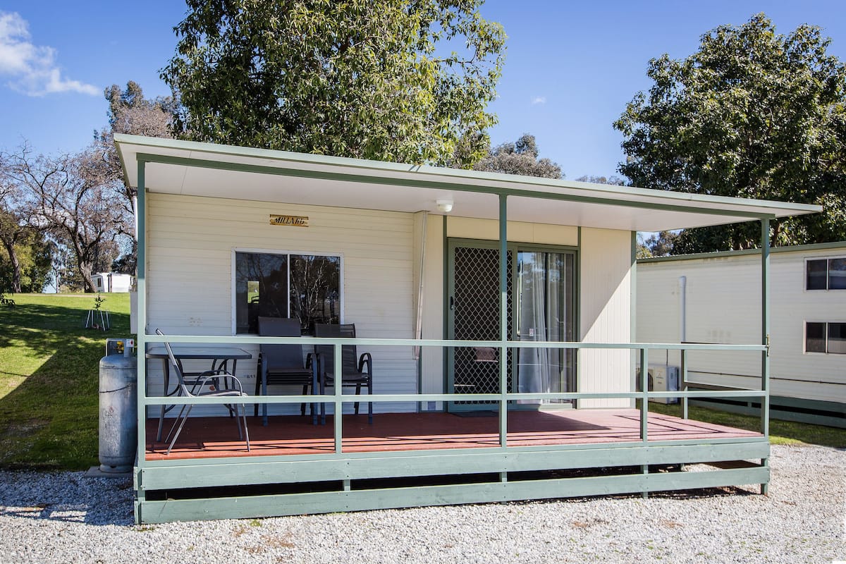 Ein kleines, eingeschossiges Gebäude mit einer überdachten Veranda, einem Tisch mit Stühlen und einem Grillplatz.