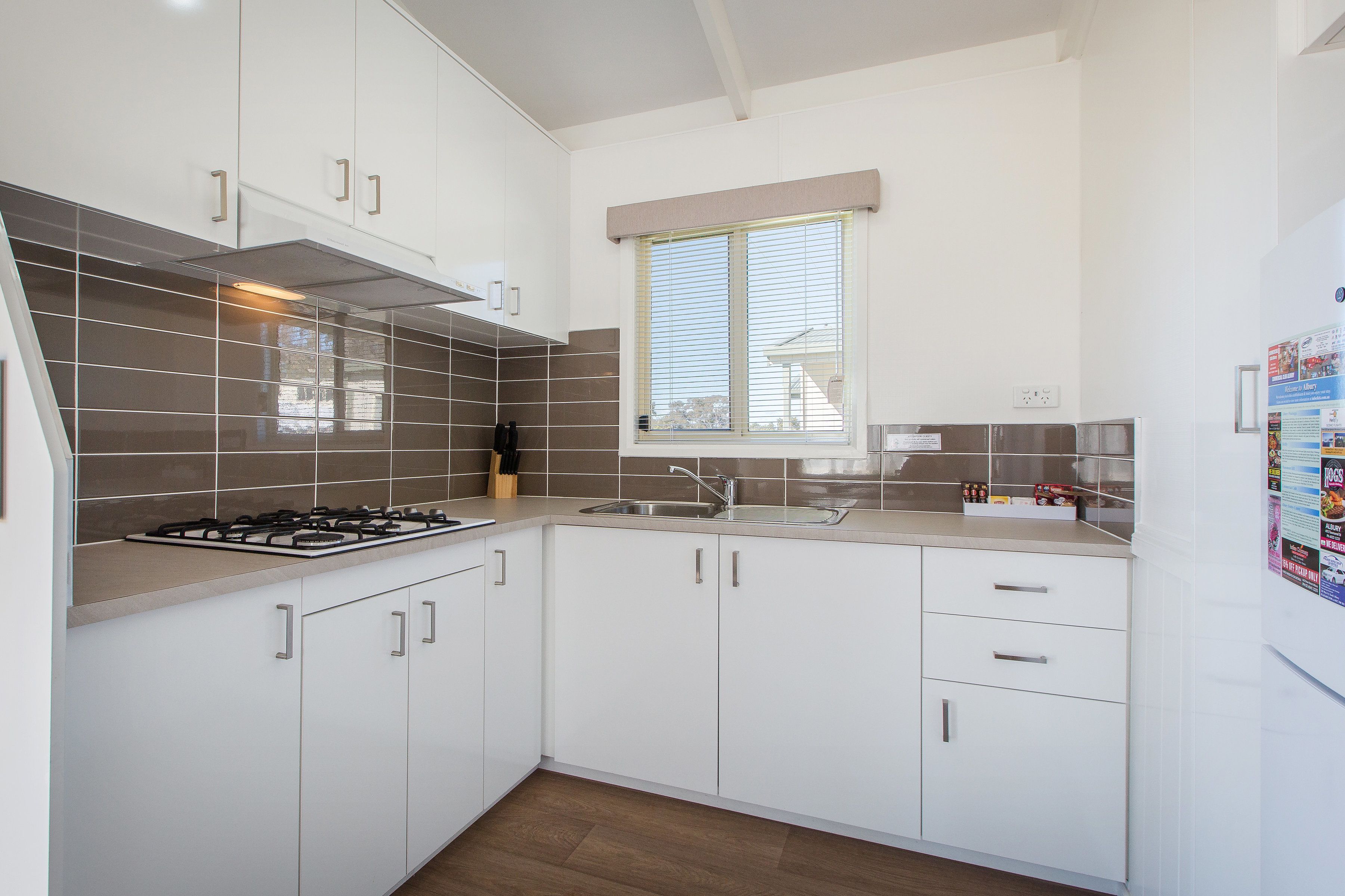 A modern kitchen with white cabinets, a gas stove, a sink, and a window with blinds.