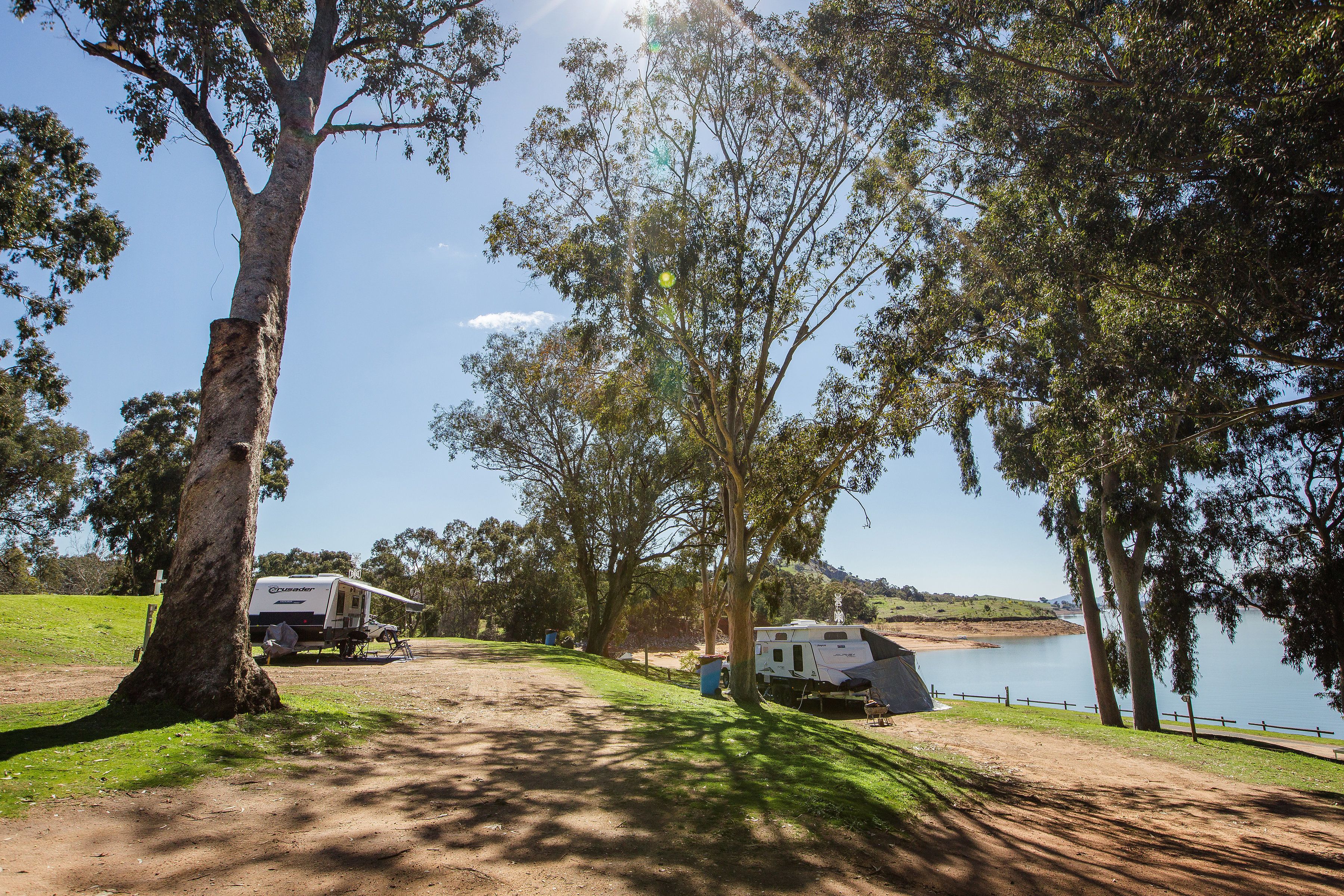 A campsite with RVs, a dirt path, and a lake.