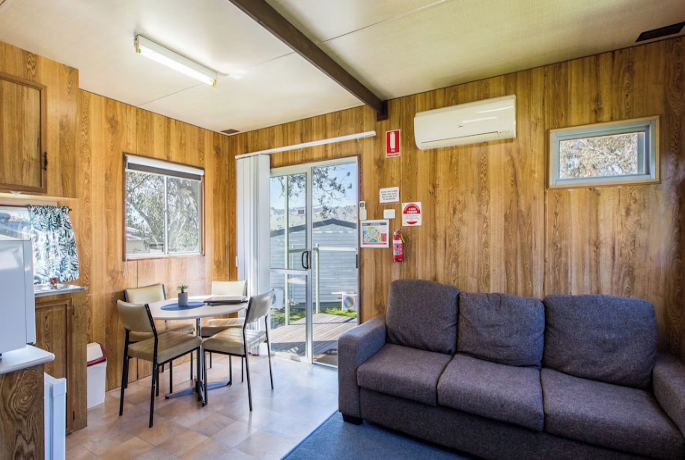 Une pièce chaleureuse avec un décor intérieur en bois, un canapé, une table à manger avec des chaises et une porte-fenêtre coulissante donnant sur l’extérieur.