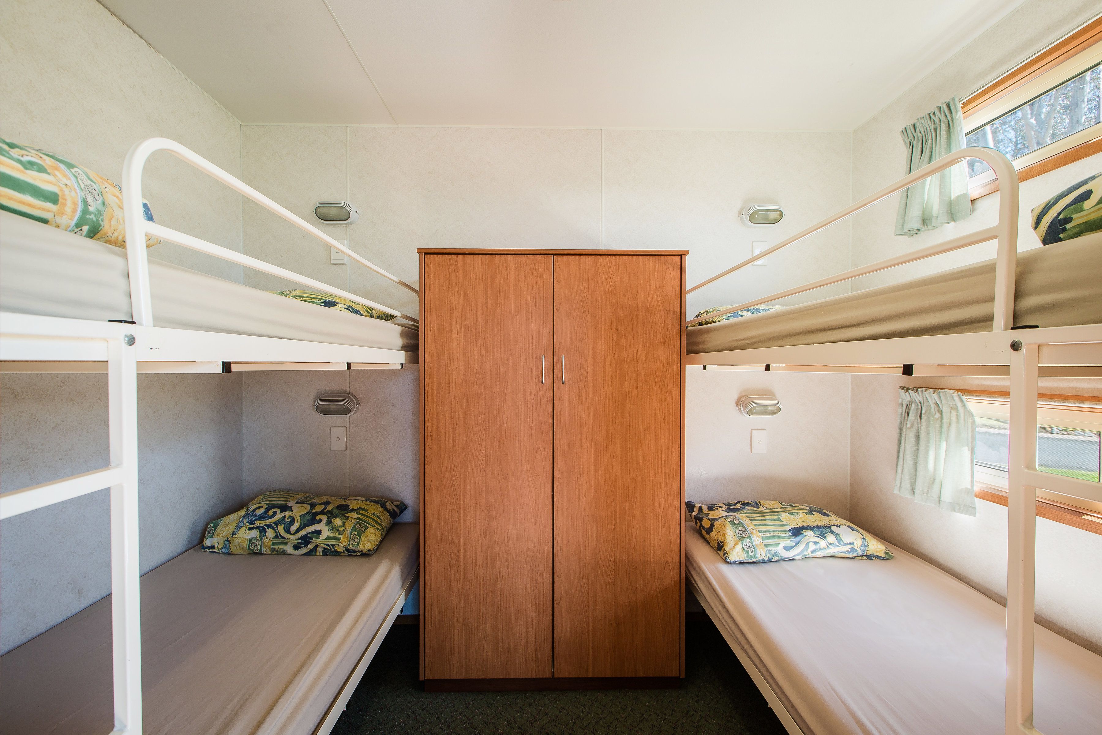 Une petite pièce avec des lits superposés, une armoire centrale et une fenêtre avec des rideaux.