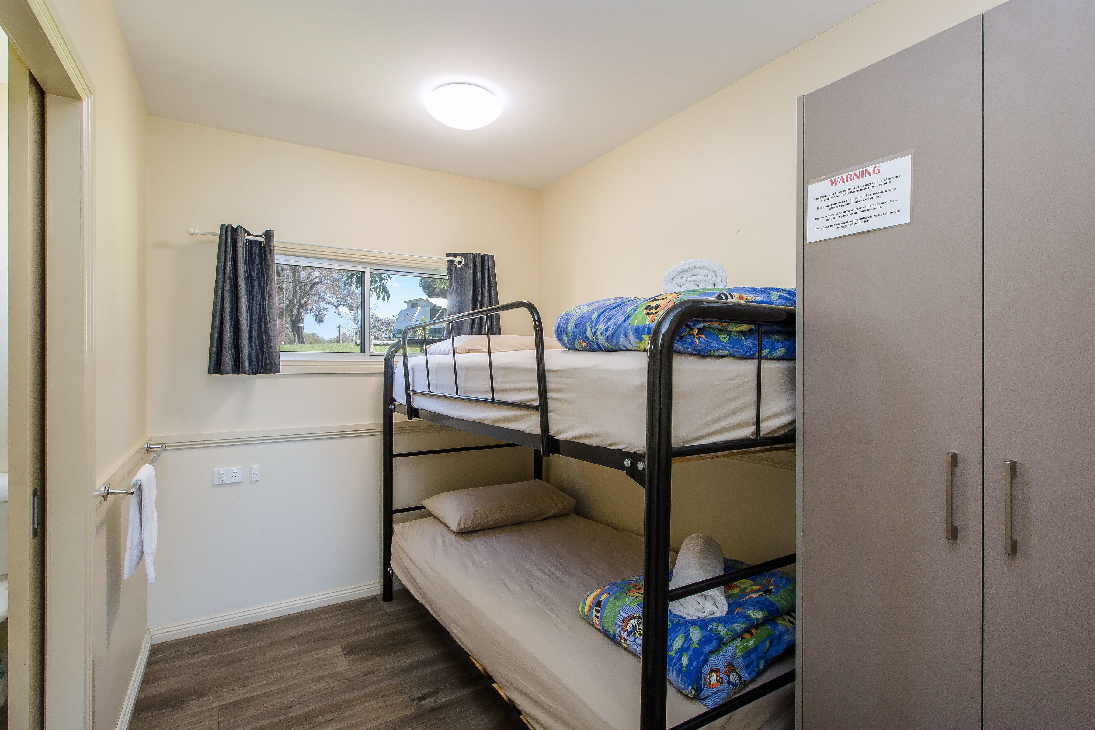 A bunk bed room with a window, a wardrobe, and a sign on the wall.