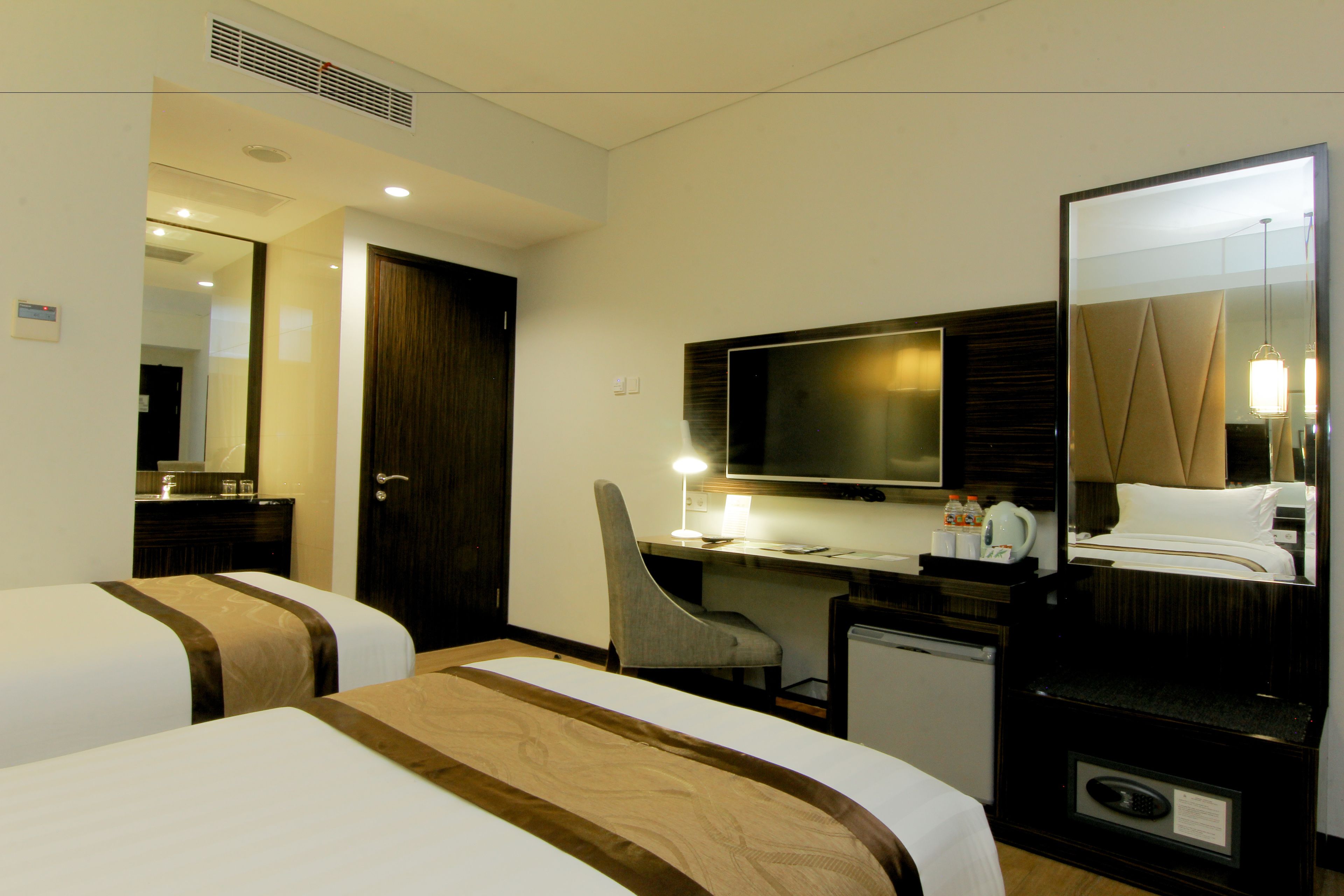 A hotel room with two beds, a desk, a chair, a television, and a mirror.
