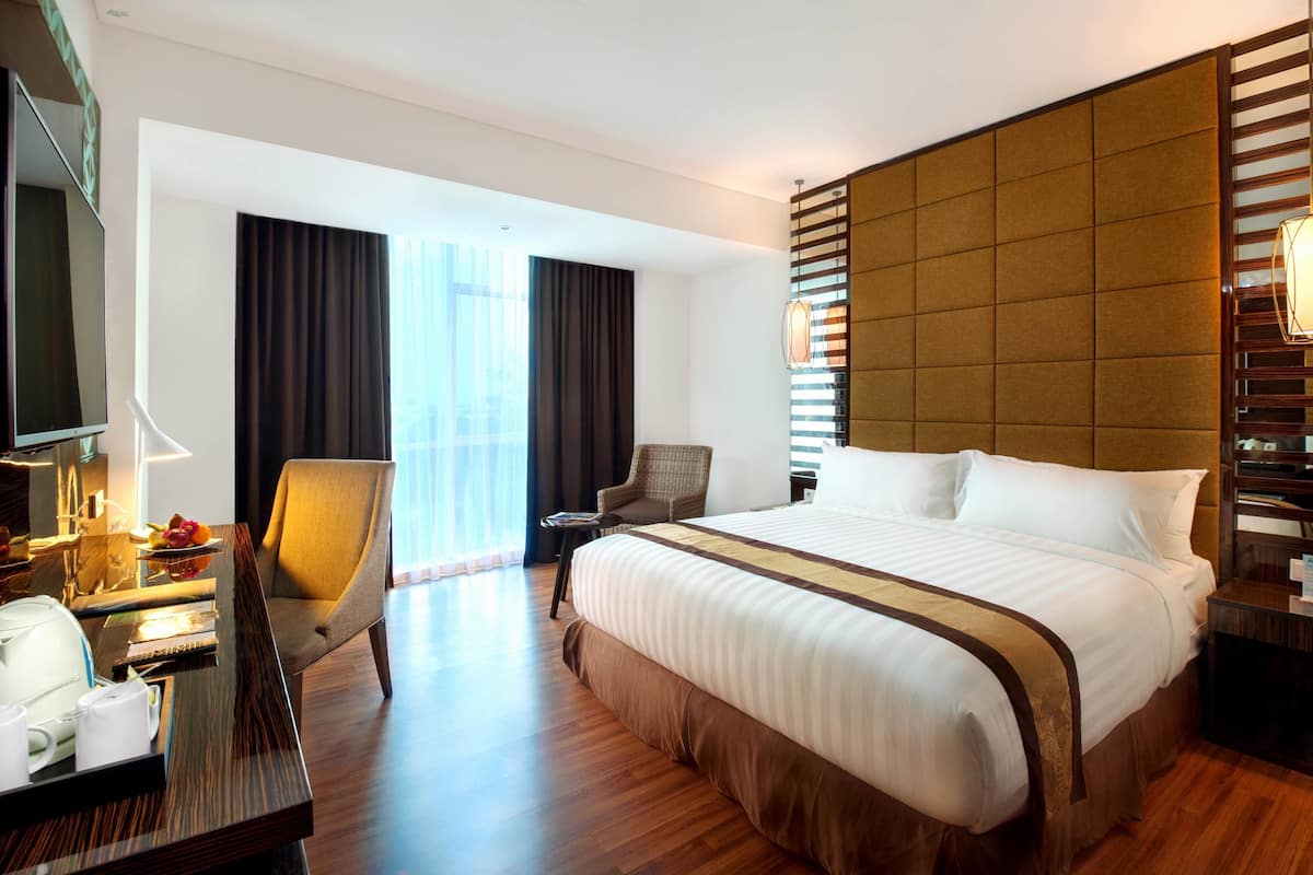 Una habitación de hotel con una cama grande, un escritorio con lámpara, una silla y un televisor.