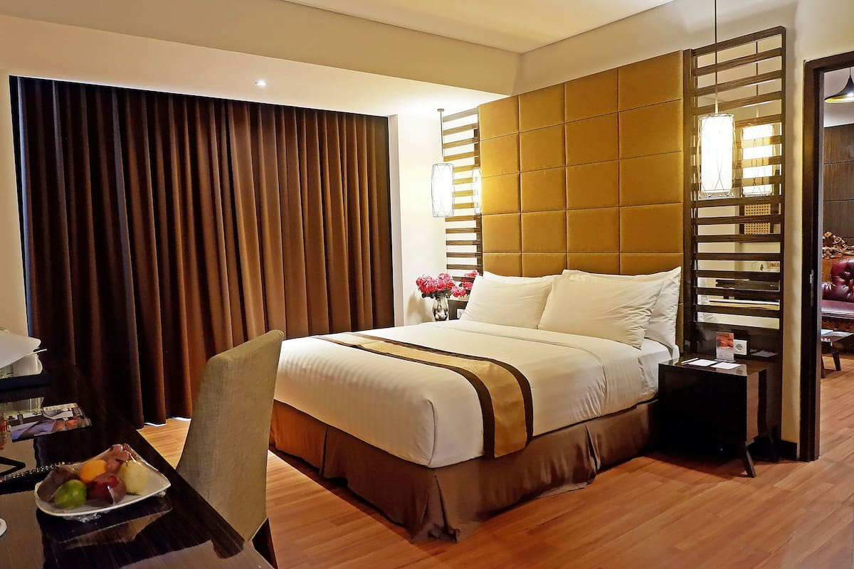 Habitación de hotel con una cama grande, suelo de madera, un escritorio con silla y una mesita de noche con lámpara.