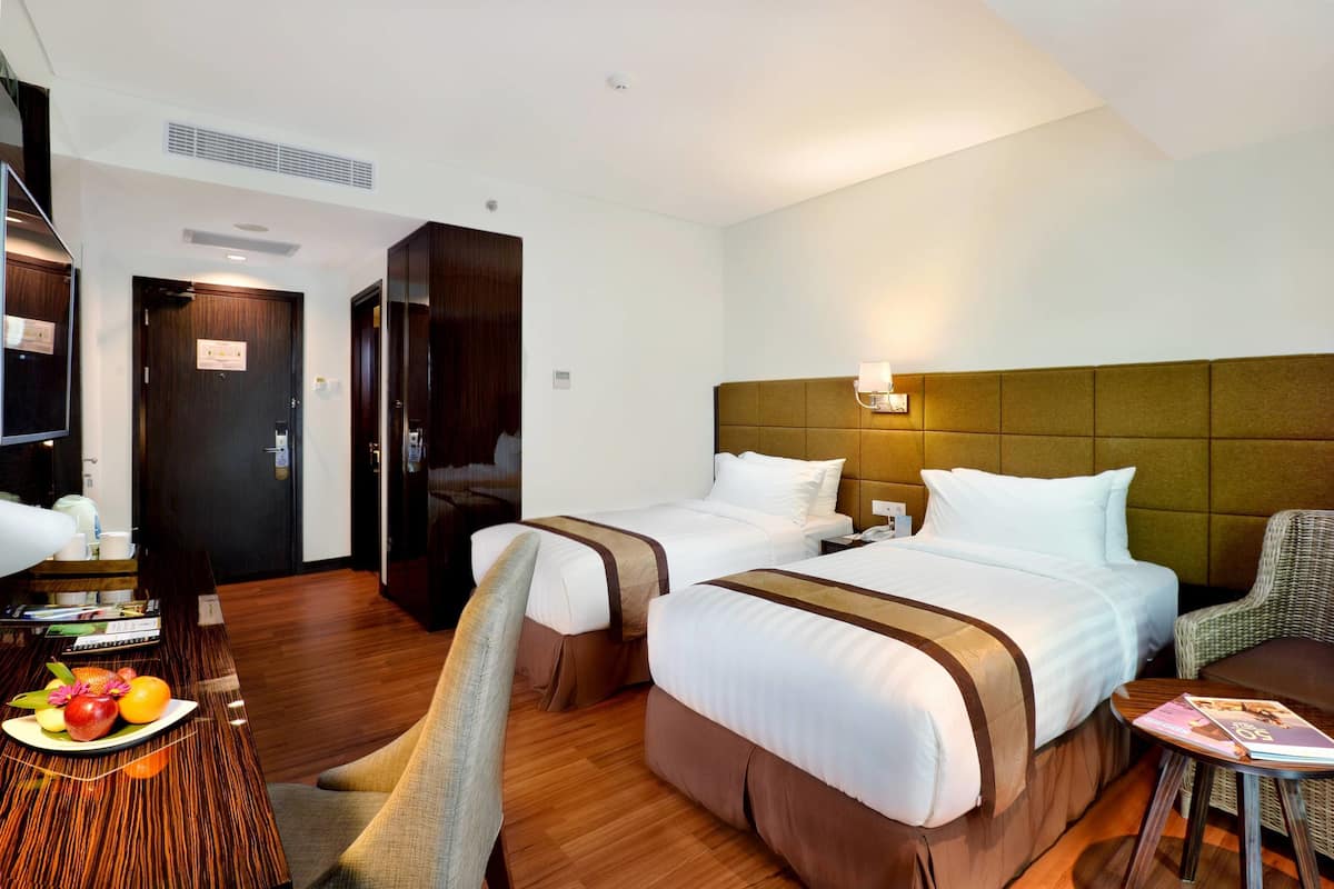 Una habitación de hotel con dos camas, piso de madera, un escritorio con silla y una mesita con una revista.