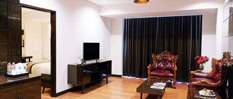 A modern living room with a flat-screen TV, dark wood furniture, a coffee table, and a large window with curtains.