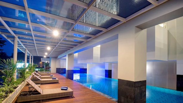 Una piscina interior con tumbonas de madera y techo de cristal.