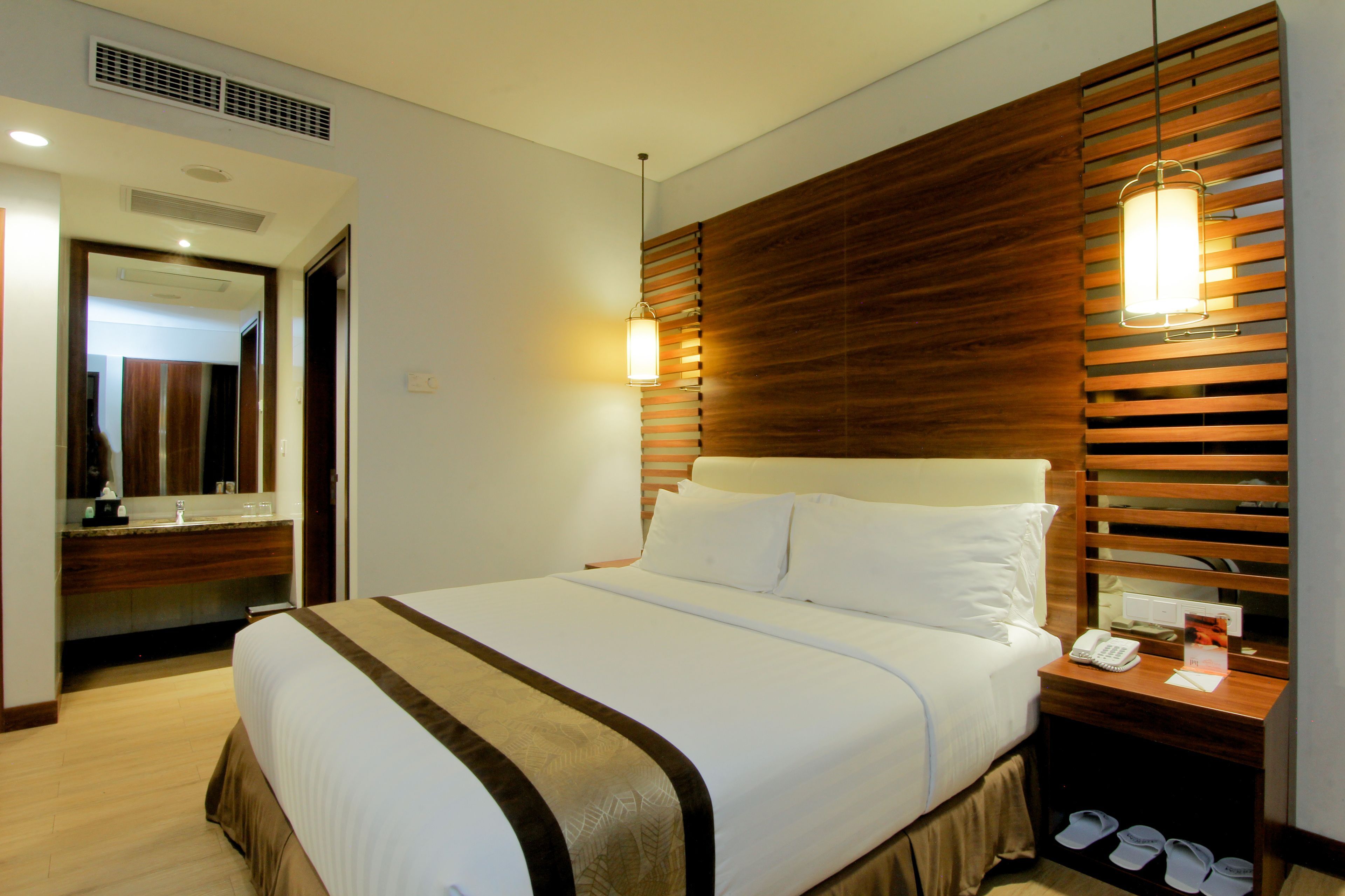 A hotel room with a large bed, wooden headboard, bedside table with a lamp, and a mirror.