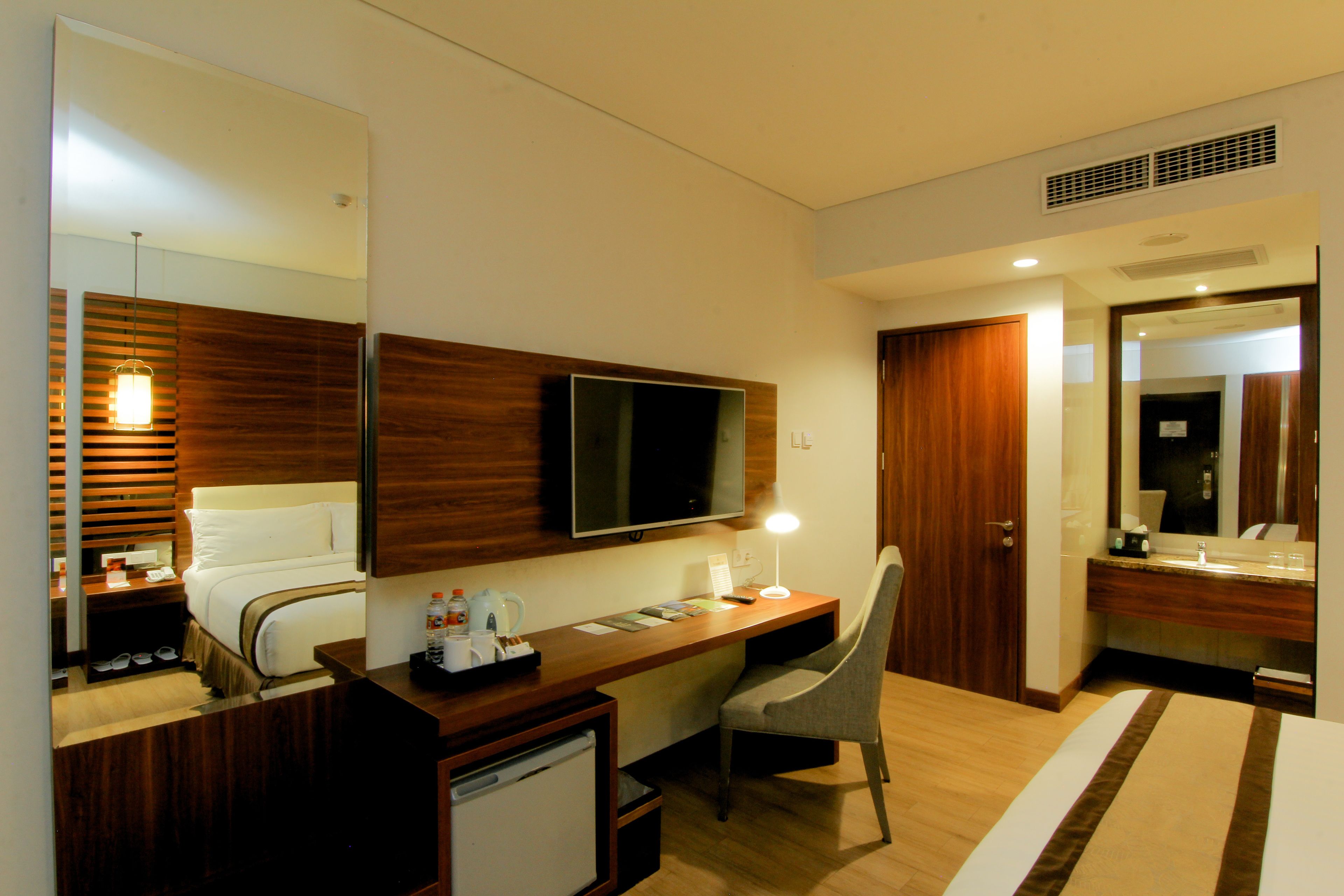 Una habitación de hotel con cama, escritorio, silla, televisor y un refrigerador pequeño.