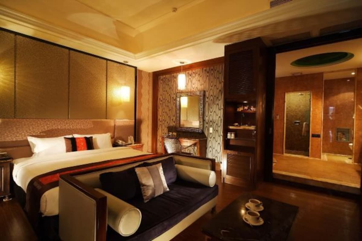 Habitación de hotel con una cama grande, un sofá, una mesa de centro, un baño con espejo y zona de ducha.