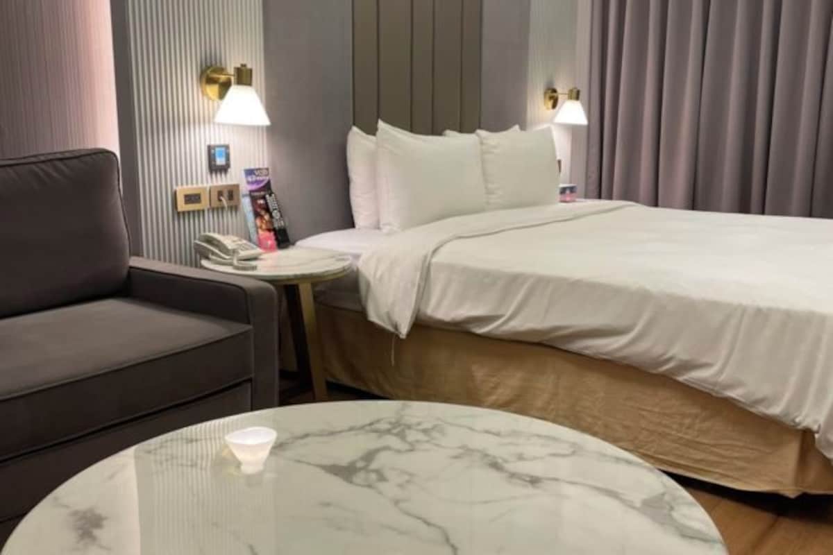 Una habitación de hotel con una cama, un sofá, una mesita y una lámpara.