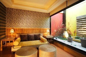 A cozy room with a sofa, two side tables, a patterned wall, and a view of a garden through a window. - Seasons Boutique Motel (Kaohsiung)