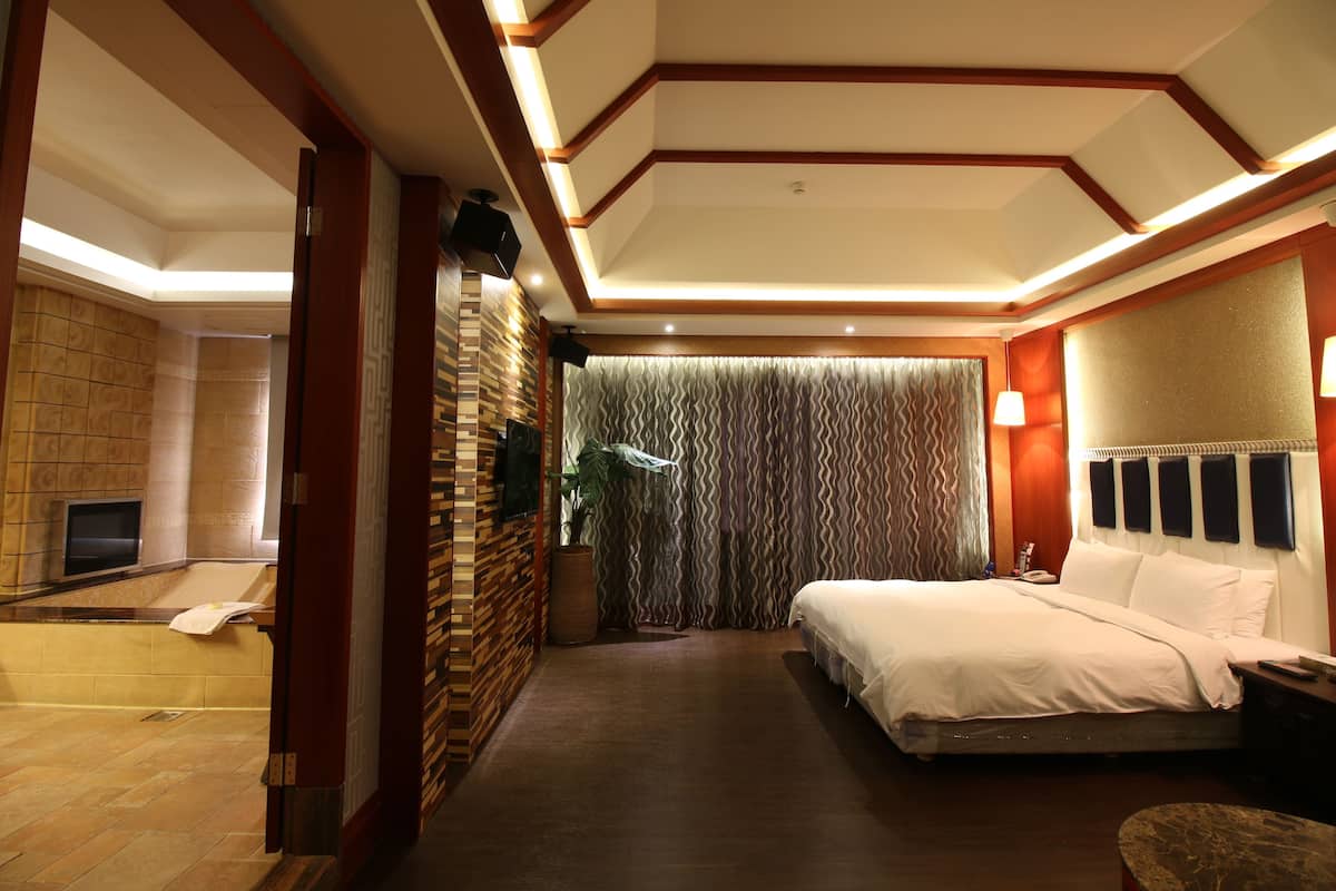 Een hotelkamer met een groot bed, een televisie, een badkamer met een badkuip en een douche.