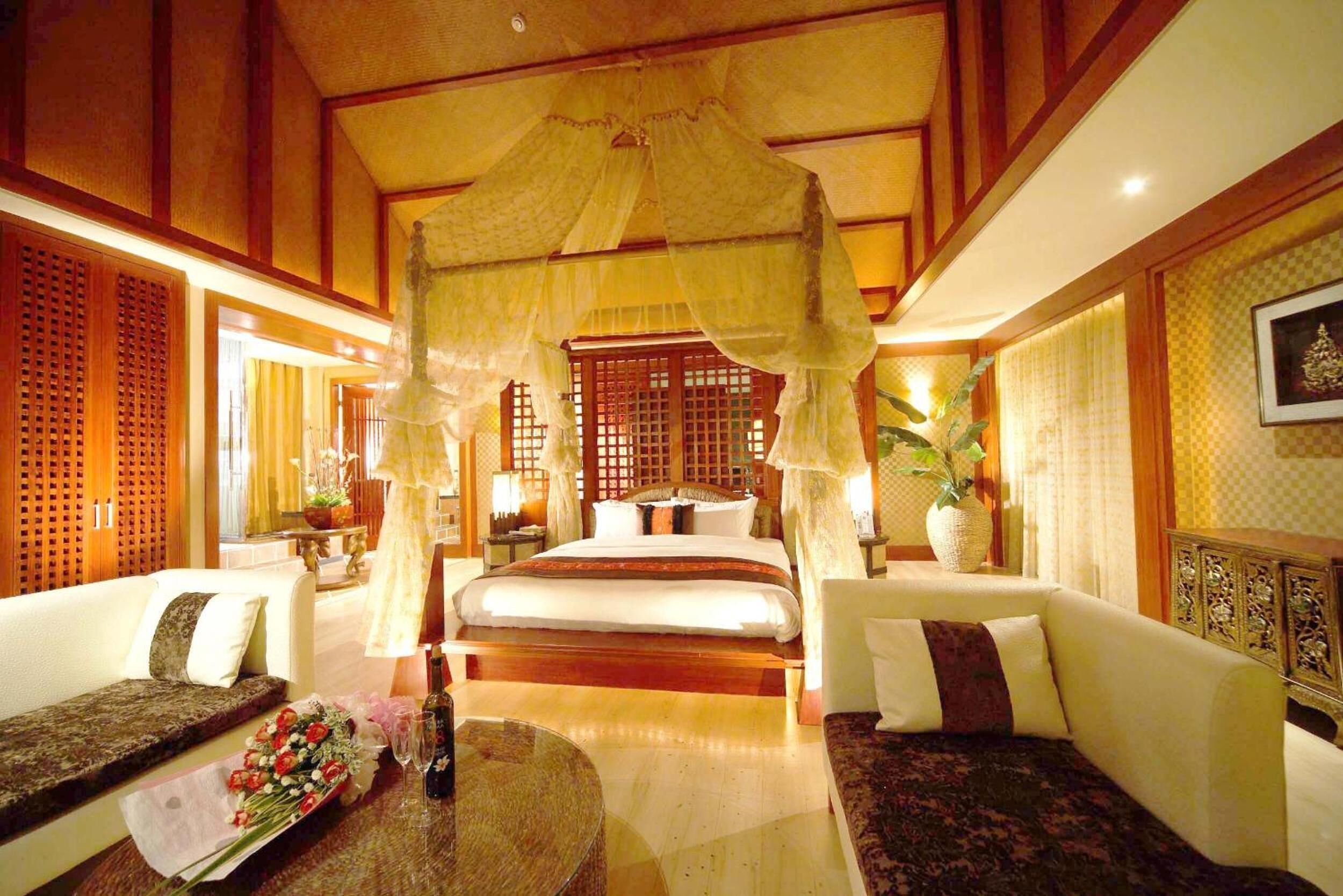 A traditional room with a bed, two sofas, a dining table with flowers, and a decorative canopy.