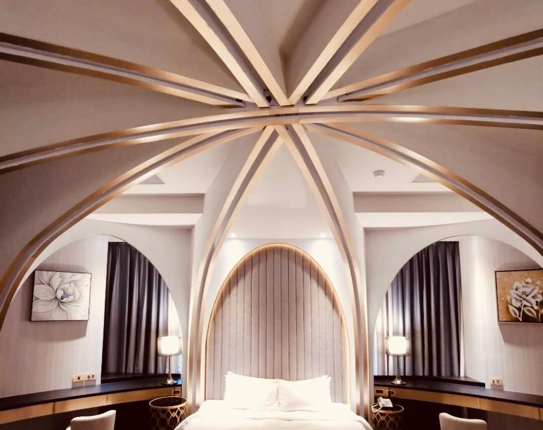 Una habitación de hotel moderna con un diseño de techo abovedado único, una cama grande y un área de descanso con una pequeña mesa y sillas.