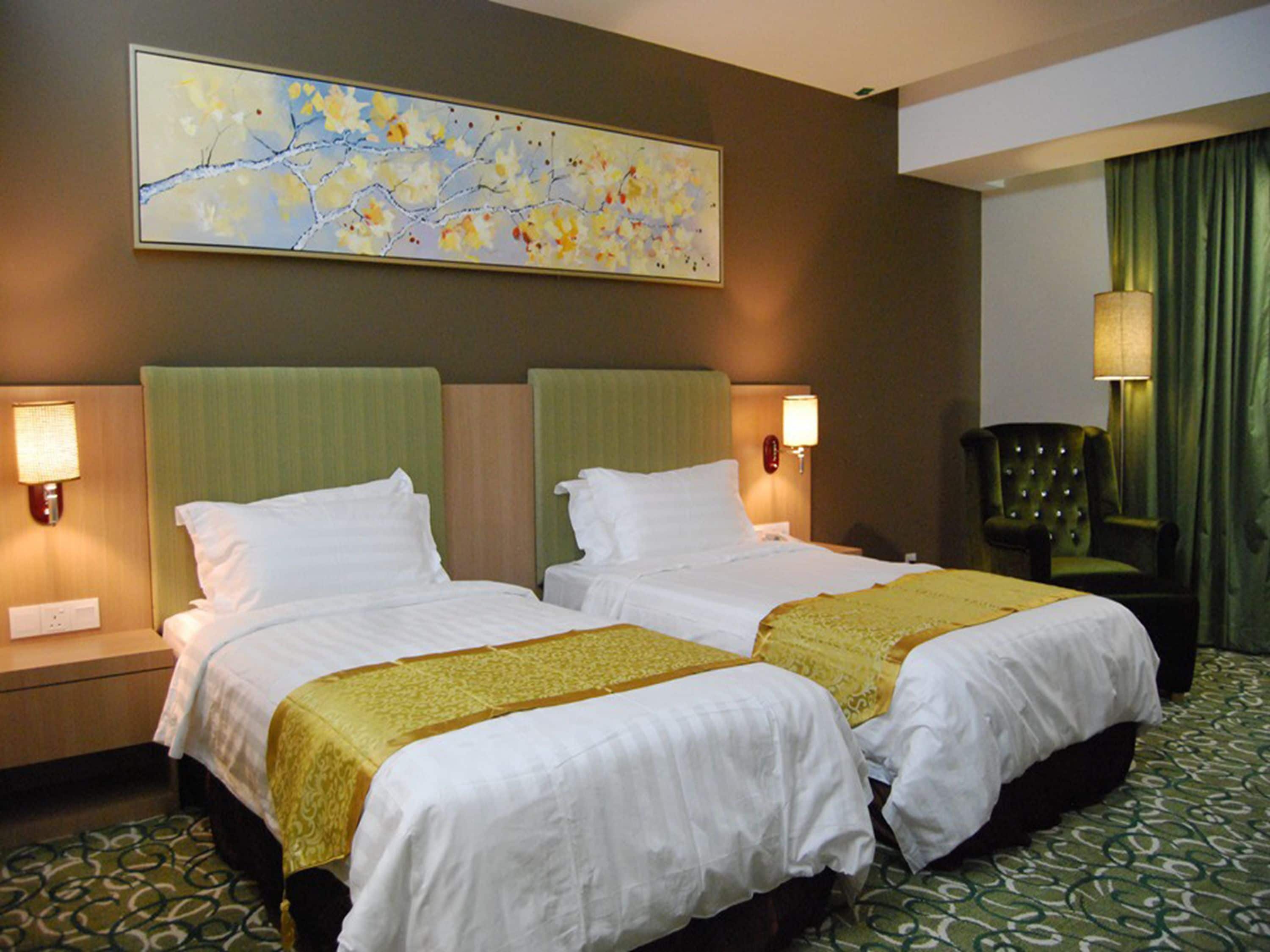A hotel room with two beds, green headboards, white bedding, a large floral painting on the wall, and a green patterned carpet.