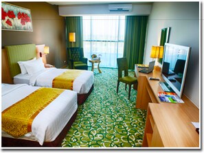 A hotel room with two beds, a desk with a computer, a TV, and a window with curtains.