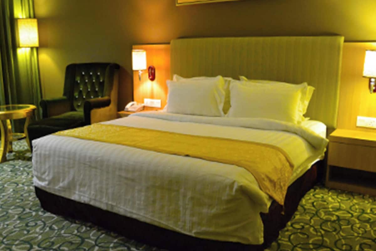 A hotel room with a large bed, a chair, a nightstand, and a lamp.