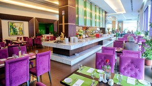 A hotel lobby with a central bar area, multiple dining tables with purple chairs, and a large painting on the wall. - Hotel Aifa (Labuan)