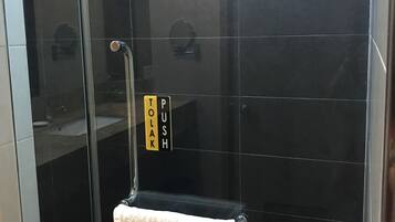 A glass-enclosed shower with a towel hanging on a rack, a push button, and a mirror.