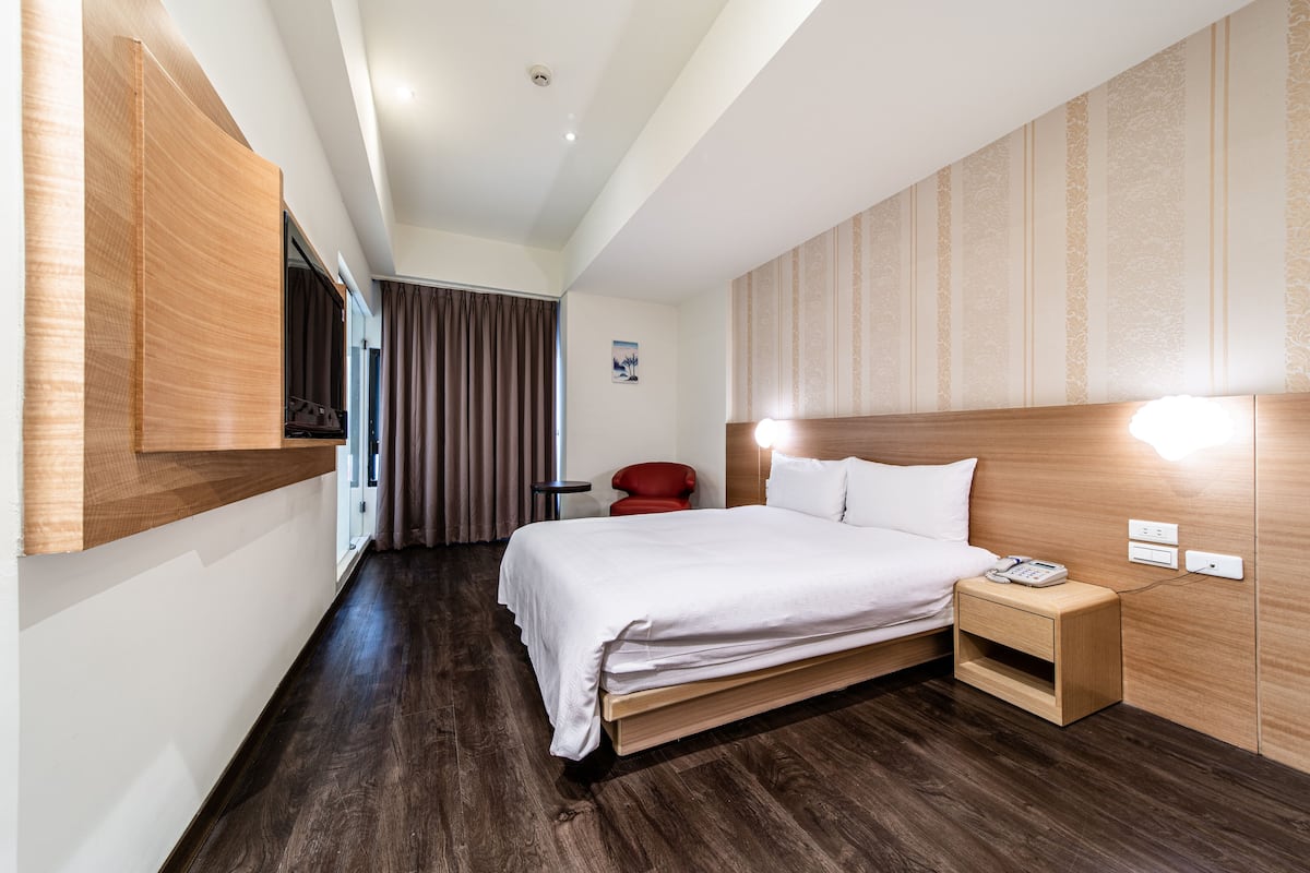 A hotel room with a wooden headboard, a bedside table with a phone, and a red chair.