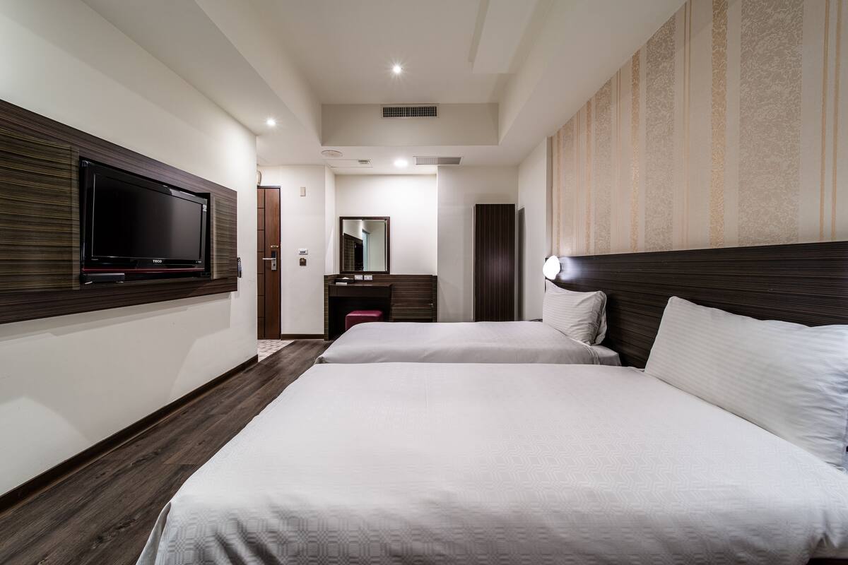 A hotel room with two beds, a TV mounted on the wall, a mirror, and a wooden headboard.
