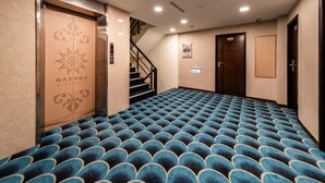Un vestíbulo de hotel con alfombra estampada, una escalera y una puerta con un emblema decorativo.