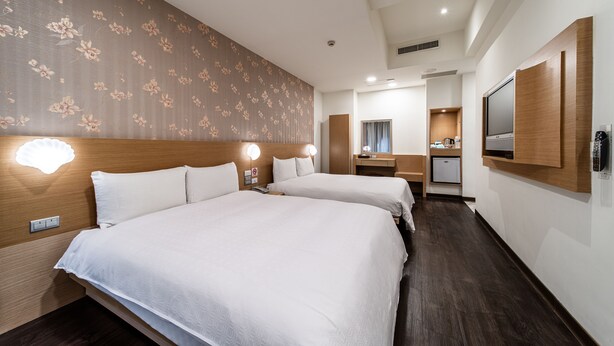 Habitación de hotel con dos camas, cabecero de madera, una kitchenette pequeña, un espejo y una lámpara en el techo.