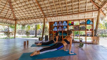 A yoga studio with wooden floors, a thatched roof, and a shelf with yoga mats and equipment.