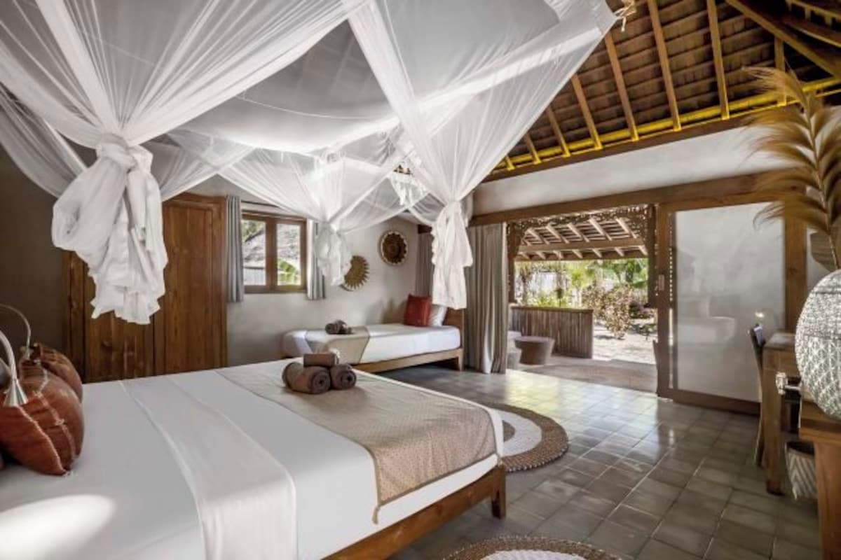 A bedroom with a canopy bed, a sitting area with a sofa, and a view of the outdoors.