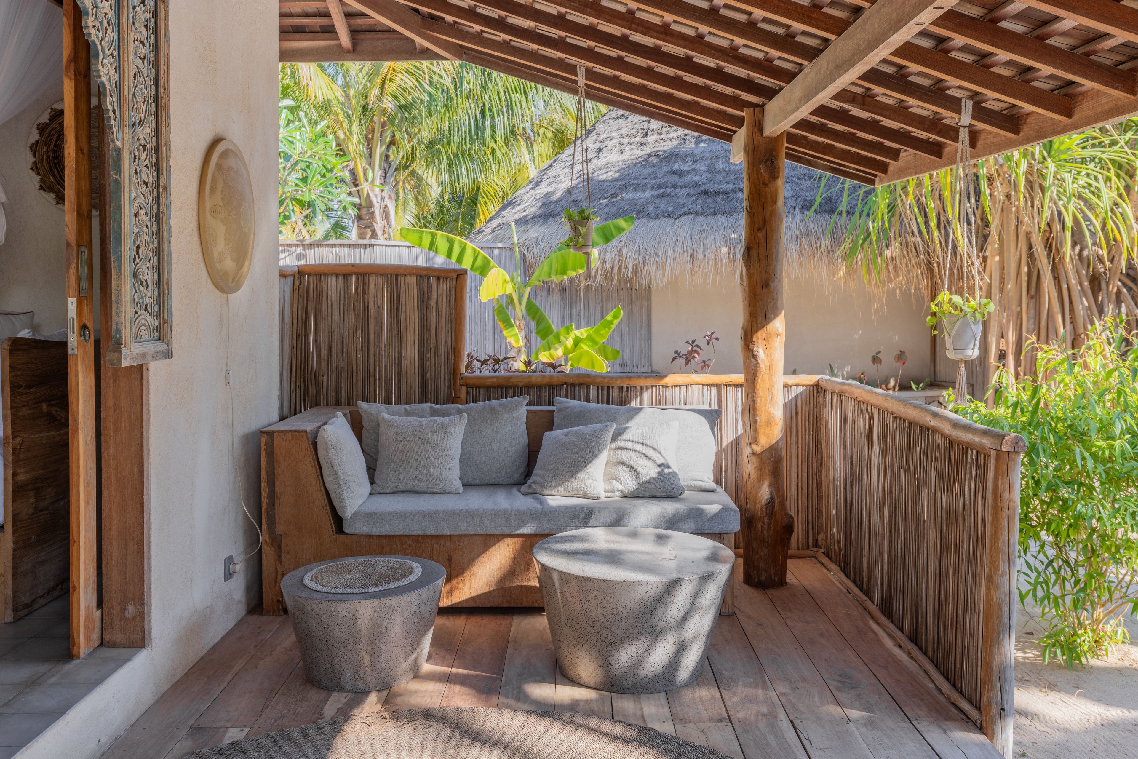 A covered outdoor seating area with a wooden bench, a cushioned sofa, and a round table.