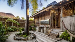 A wooden deck with a stone planter, a wooden bench, and a stone table. - SEED Resort (Rote Island)