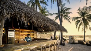 A beachside bar with a thatched roof, bar stools, and a view of the ocean. - SEED Resort (Rote Island)