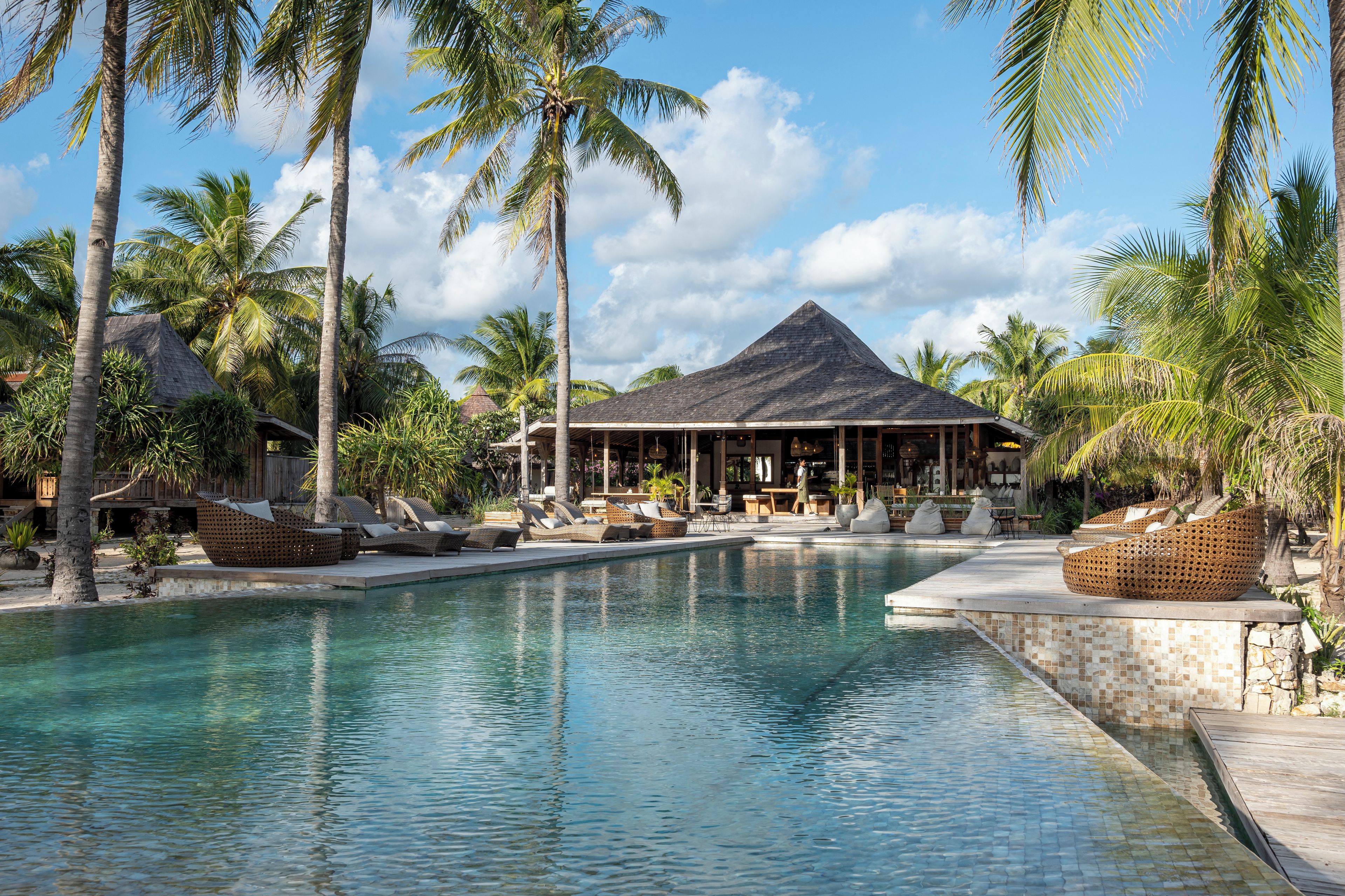 Um resort com piscina, espreguiçadeiras e um prédio com telhado de palha.
