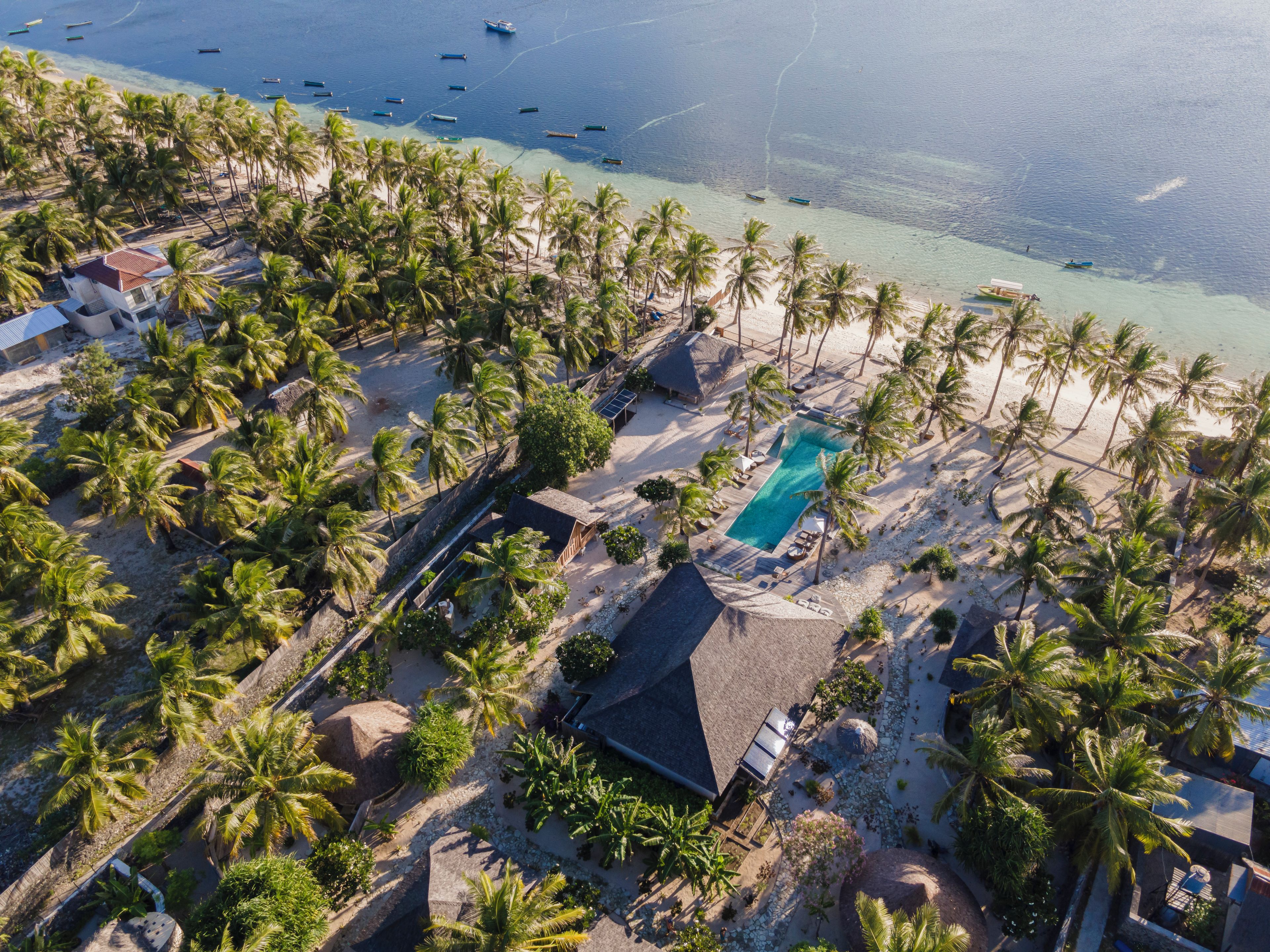 Luftaufnahme eines Resorts mit Schwimmbad, Palmen und Strand.