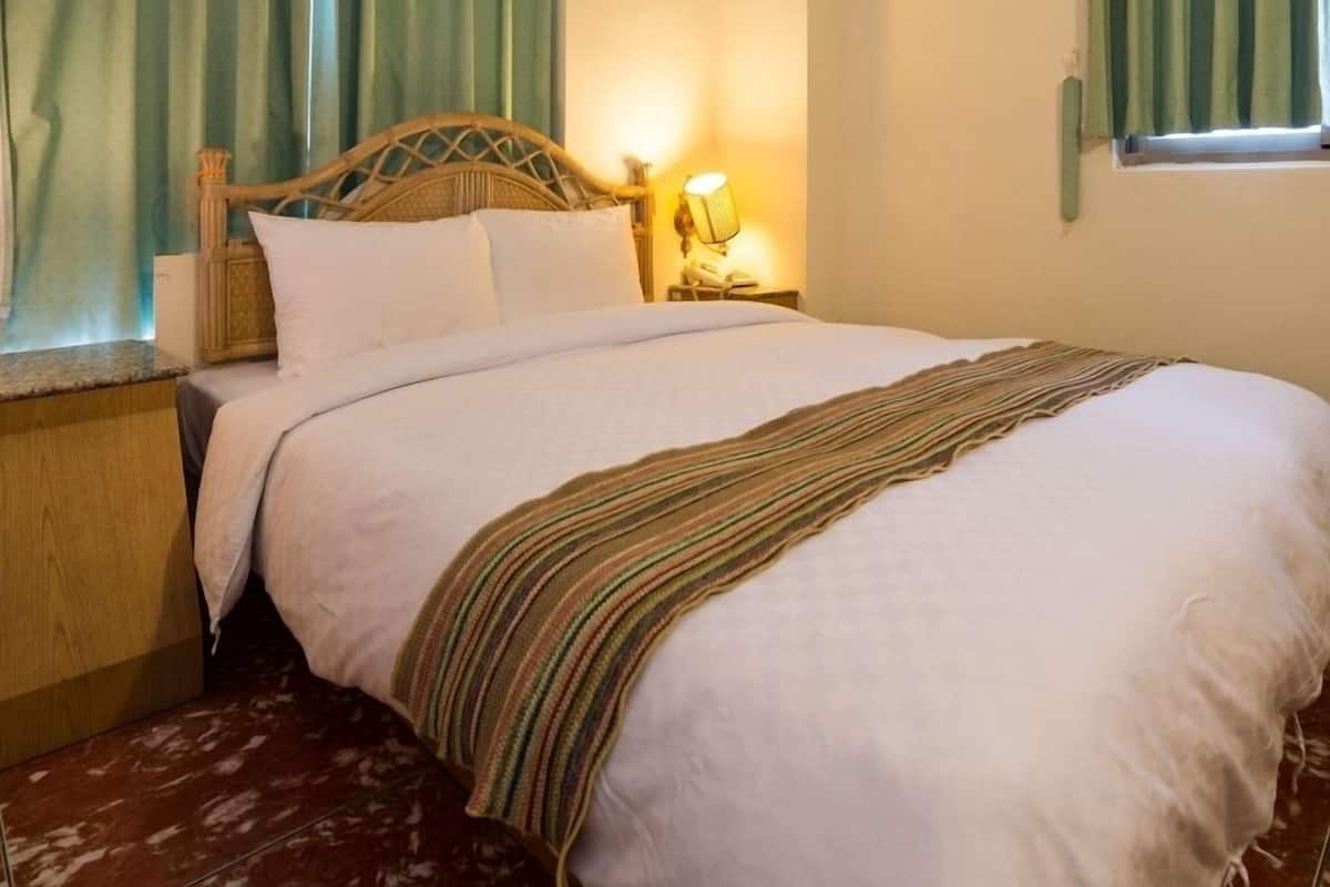 A neatly made bed with a striped blanket, a wooden headboard, and a bedside lamp.