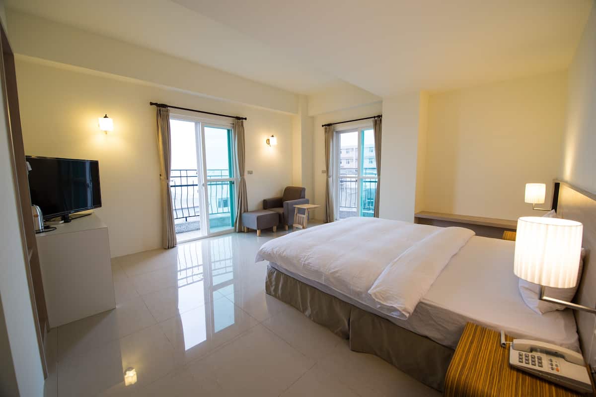 A hotel room with a bed, a TV, a desk, and a balcony.