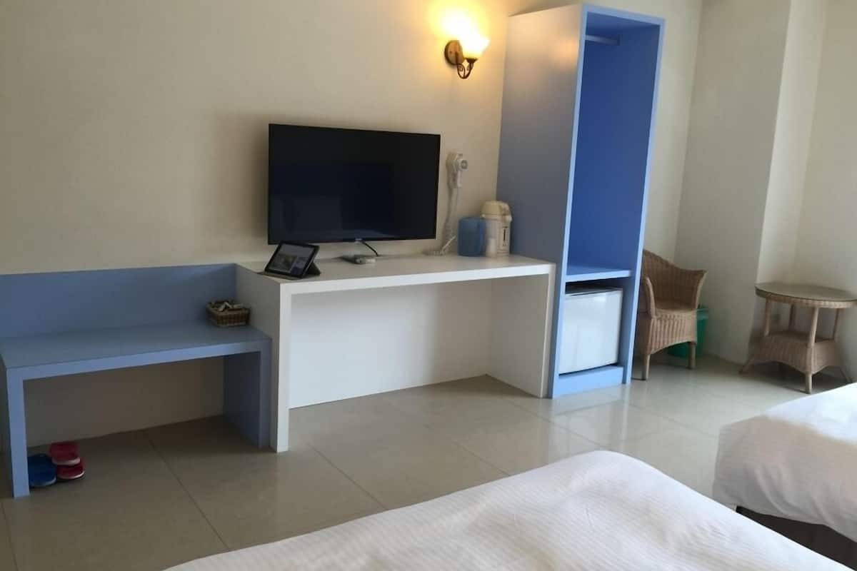 A hotel room with a bed, a desk with a TV, a chair, and a small table.