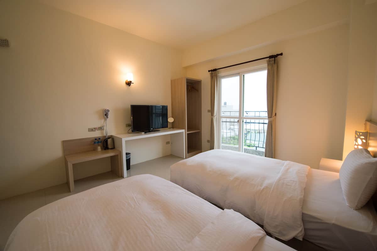 A hotel room with two beds, a TV, a desk, and a window with a view.