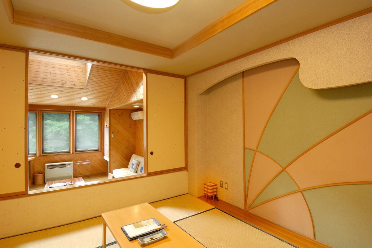 A traditional Japanese room with tatami flooring, a low table, a window with a view of greenery, and sliding doors.