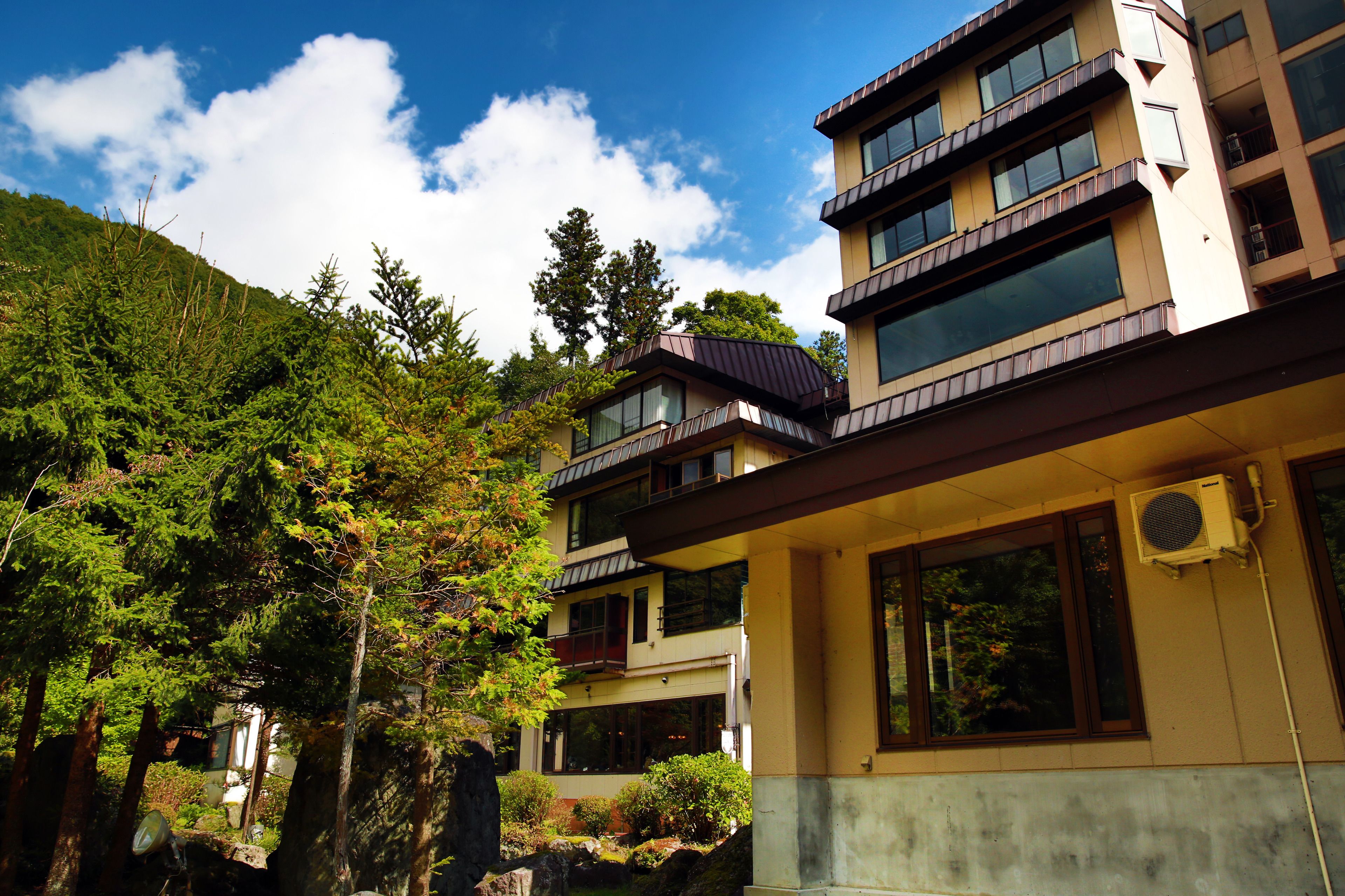 A multi-story hotel with balconies, large windows, and a mountainous backdrop.