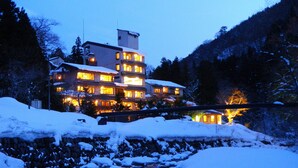 Un immeuble à plusieurs étages avec des fenêtres illuminées, entouré d’un paysage enneigé et d’une rivière.