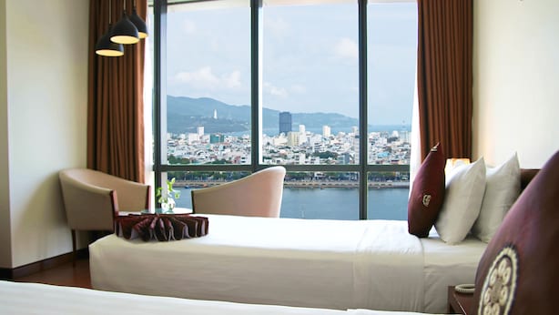 Una habitación de hotel con un ventanal grande, una cama, una silla y una mesa con un jarrón.