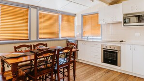A kitchen with wooden cabinets, a built-in oven, and a dining table with chairs. - Apple Blossom Cottage (Stanthorpe)