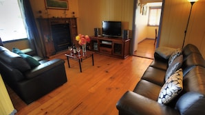 A living room with a fireplace, leather sofas, a coffee table with wine glasses, and a television. - Apple Blossom Cottage (Stanthorpe)
