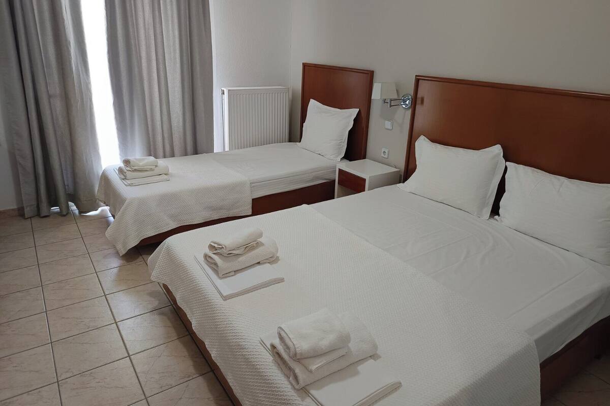 A hotel room with two beds, a radiator, a nightstand, and a window with curtains.