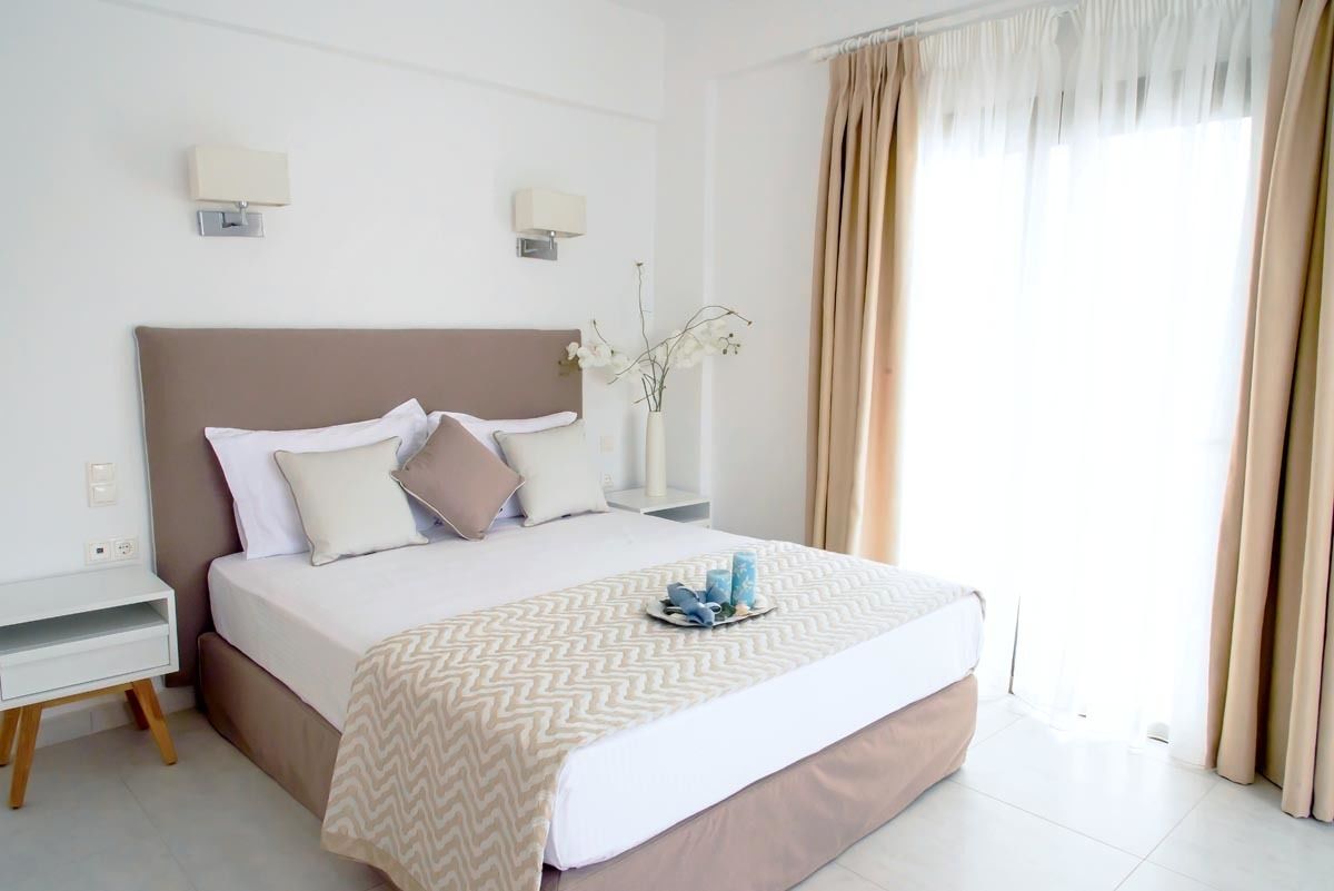 A neatly arranged hotel room with a bed, bedside tables, a vase with flowers, and a window with curtains.