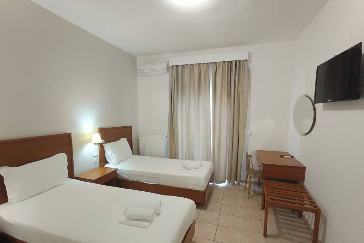 A hotel room with two beds, a desk, a chair, a TV, and a window with curtains.