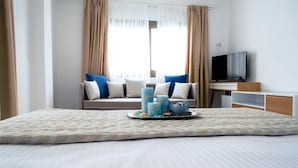 A hotel room with a bed, a TV, a sofa with cushions, and a window with curtains. - Stavros Beach Hotel (Volvi)